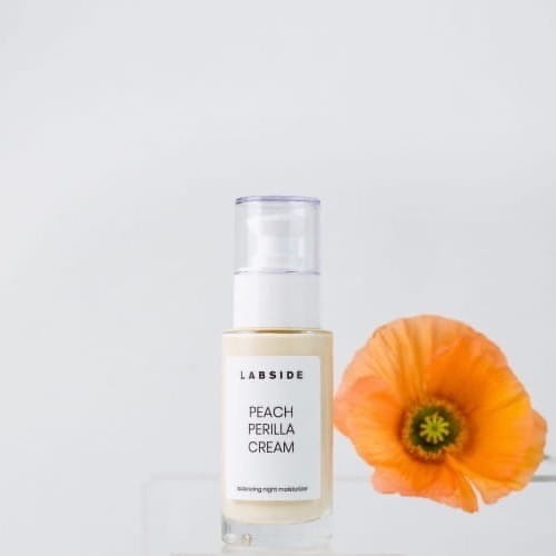 Słoiczek kremu na noc Peach Perilla Cream Labside obok połówki brzoskwini
