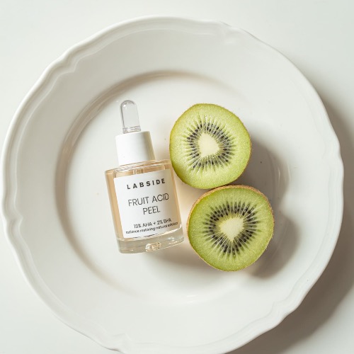 Szklana buteleczka z pipetą zawierająca peeling LABSIDE Fruit Acid Peel, leżąca na białym, ozdobnym talerzu obok dwóch przekrojonych połówek świeżego kiwi.