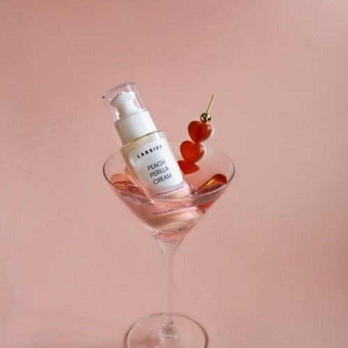 Krem LABSIDE Peach Perilla Cream w kieliszku do martini na różowym tle.